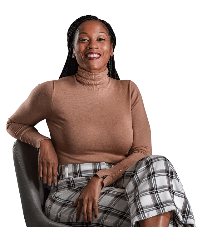 Julia Rock poses warmly with a confident smile, seated in a chair wearing a tan turtleneck and plaid pants against a navy background.